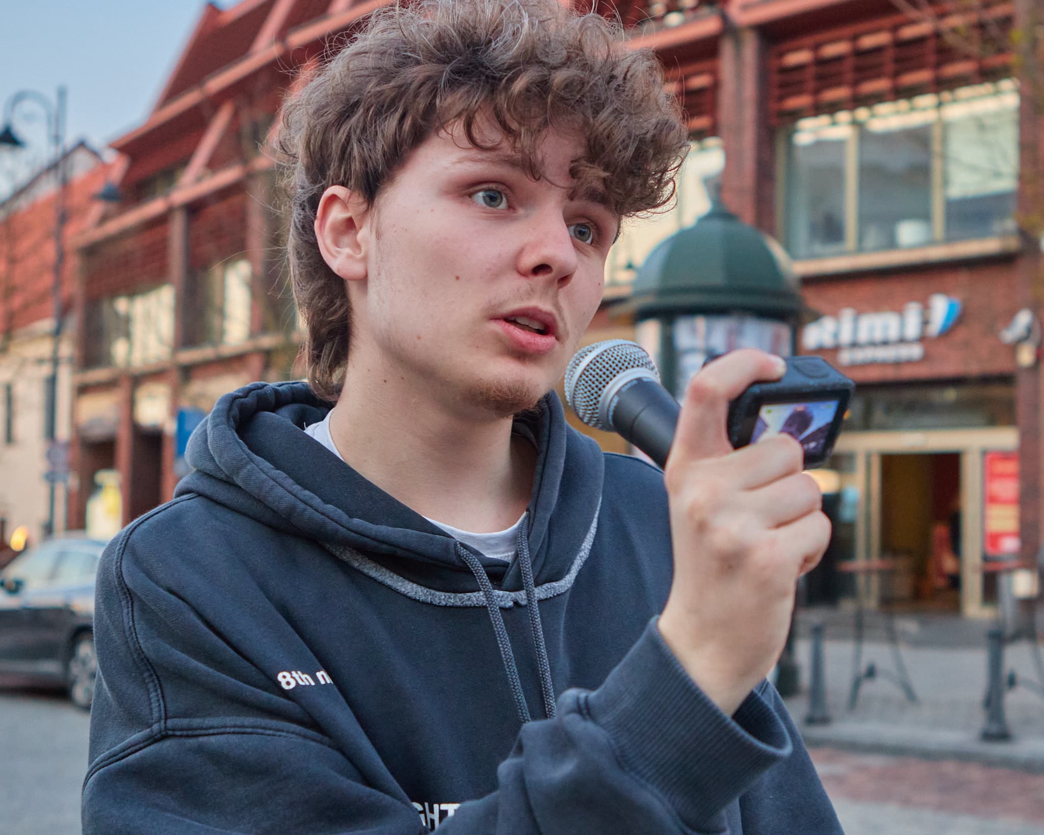 Jaunas vyras su mikrofonu kalba Vilniaus senamiesčio gatvėje