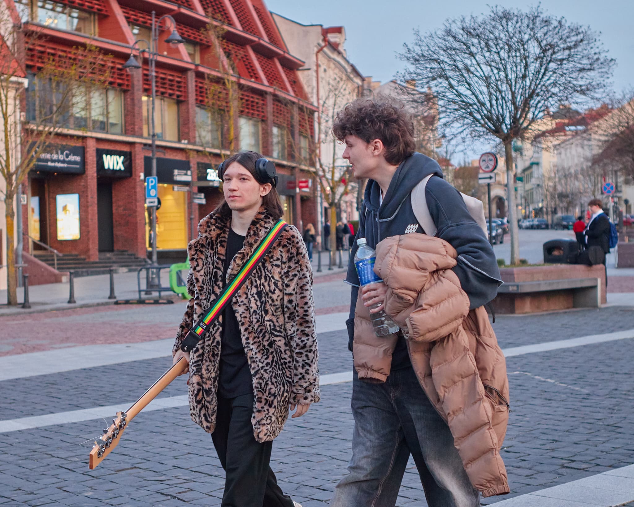 Du jauni muzikantai eina Vilniaus gatve, vienas nešasi gitarą