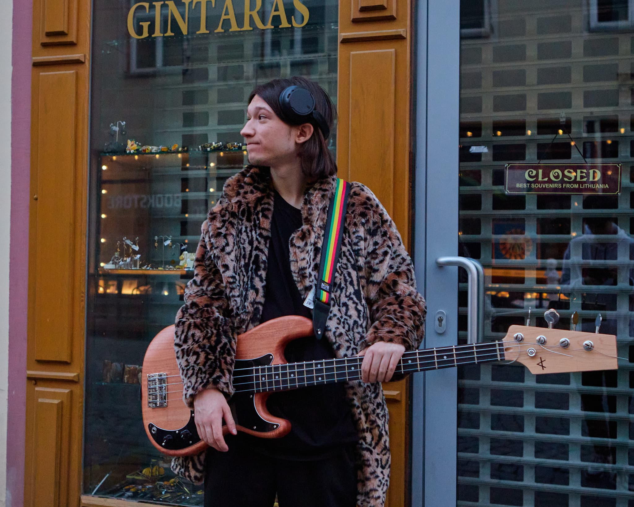 Muzikantas su bosine gitara stovi prie parduotuvės vitrinos