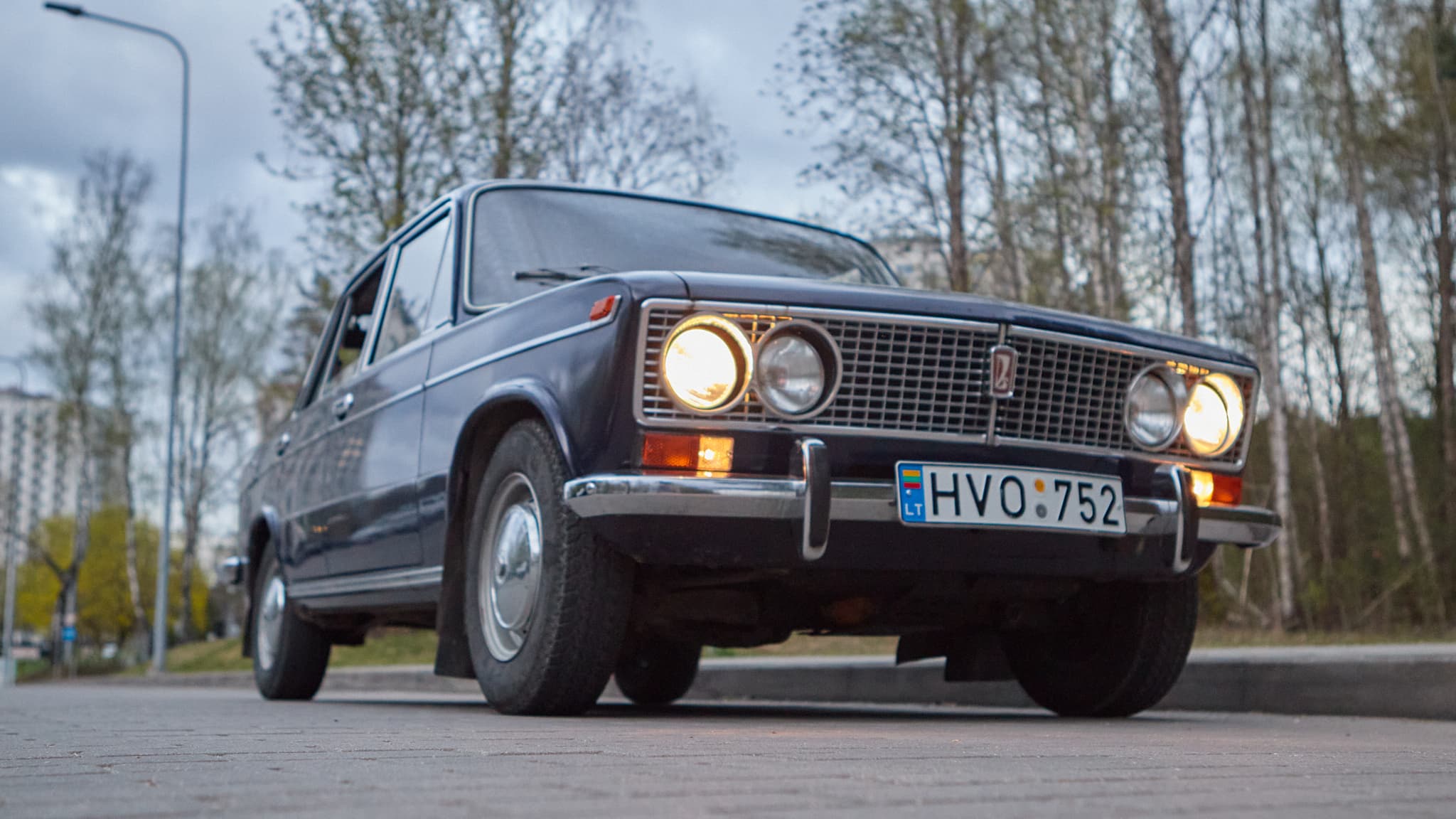 Tamsus klasikinis automobilis nufotografuotas iš žemo kampo su įjungtais žibintais