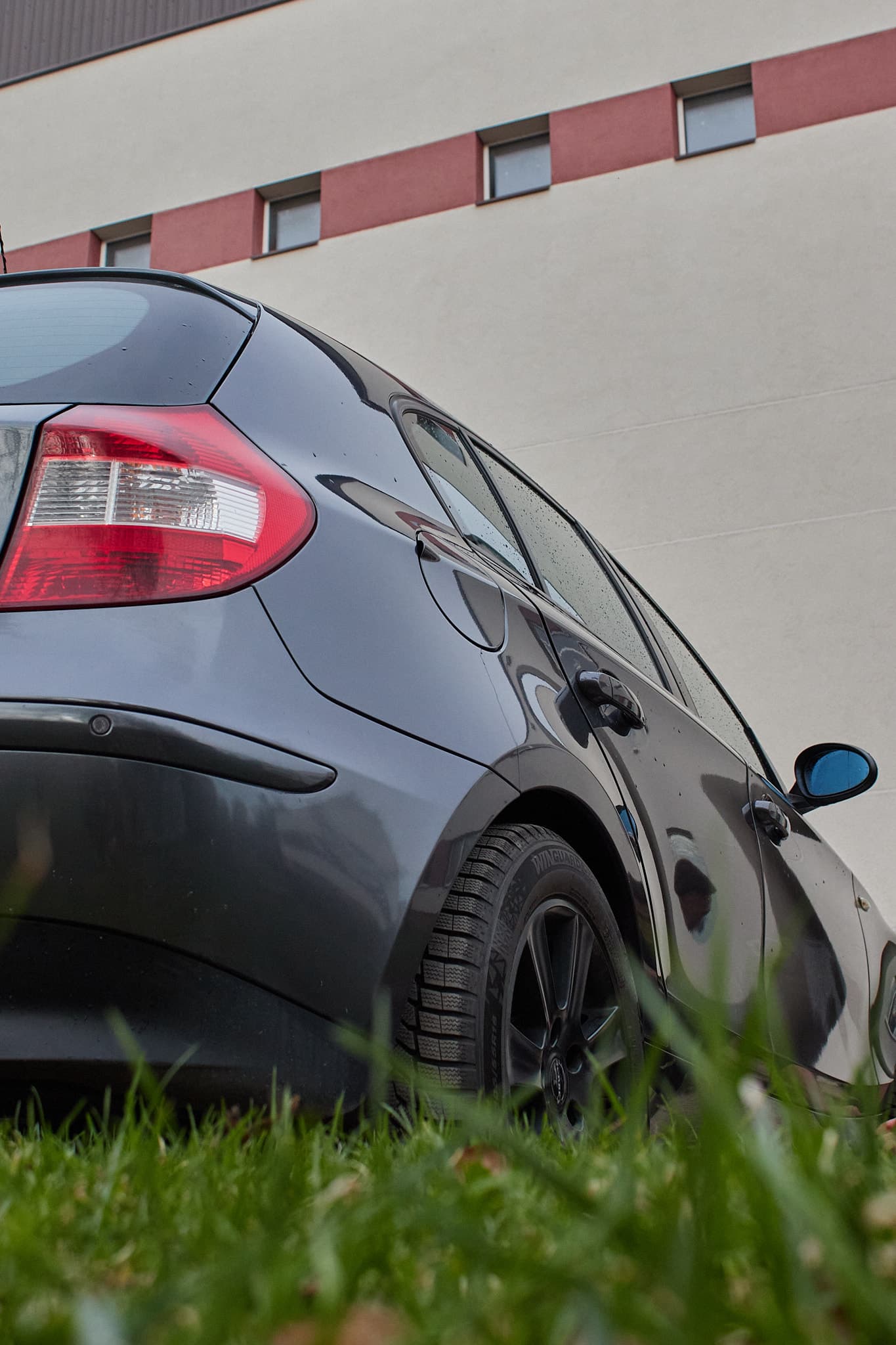 Pilko automobilio galinė šoninė dalis nufotografuota iš žemo kampo prie pastato