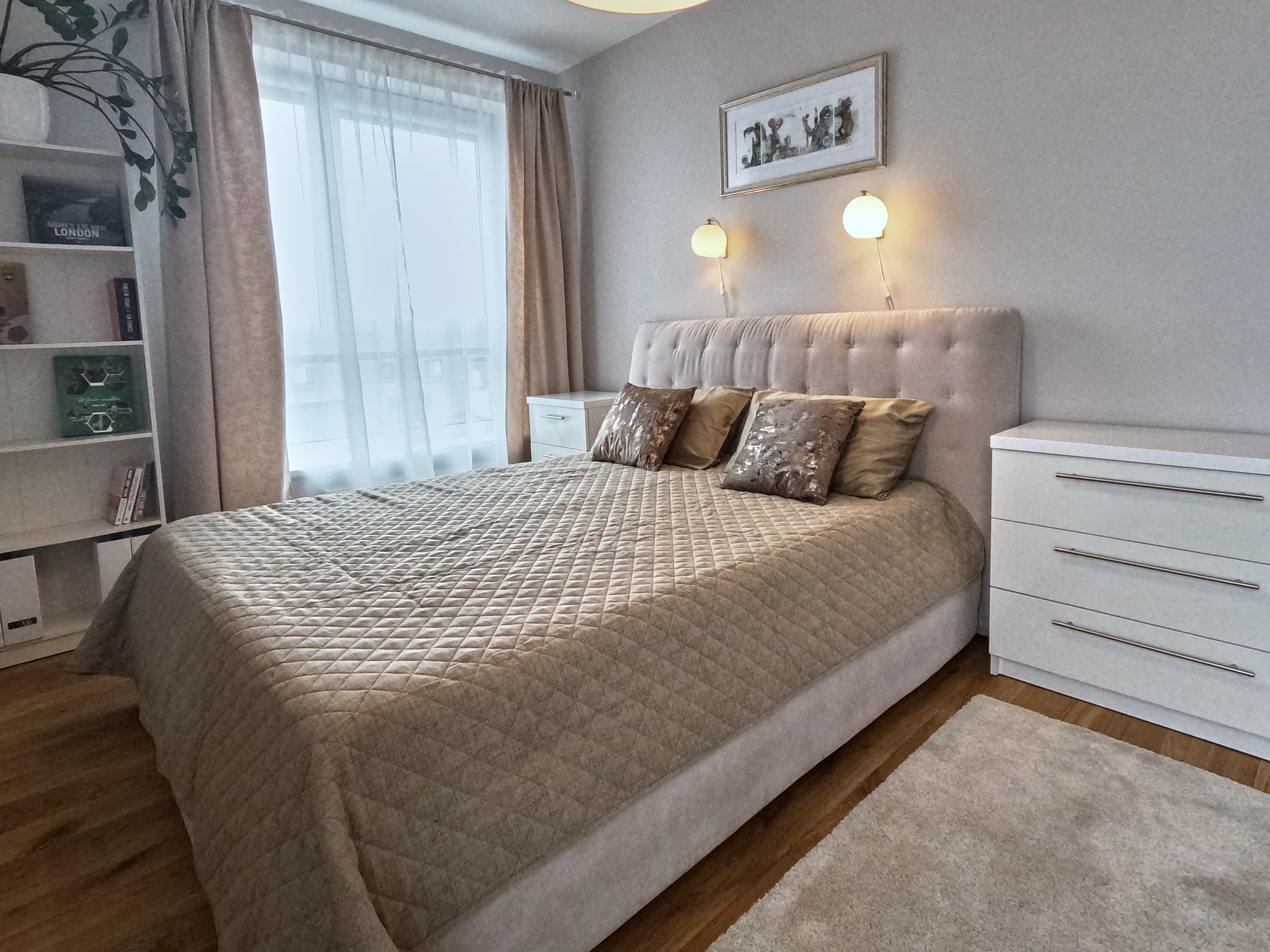 Tvarkingas šviesių tonų miegamasis su didele lova ir naktinėmis spintelėmis