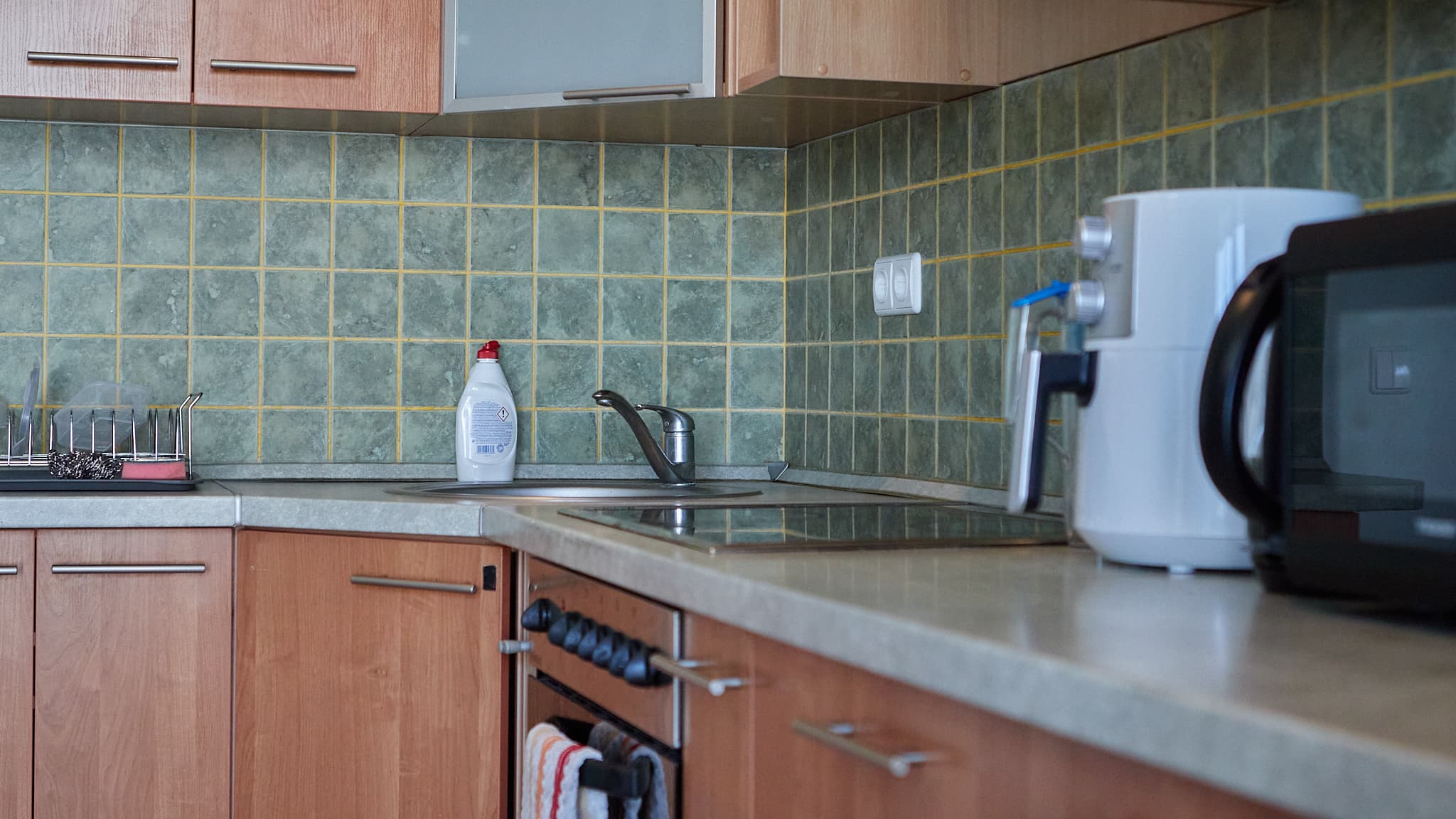 Kompaktiška virtuvė su mediniais fasadais, kriaukle ir buitine technika