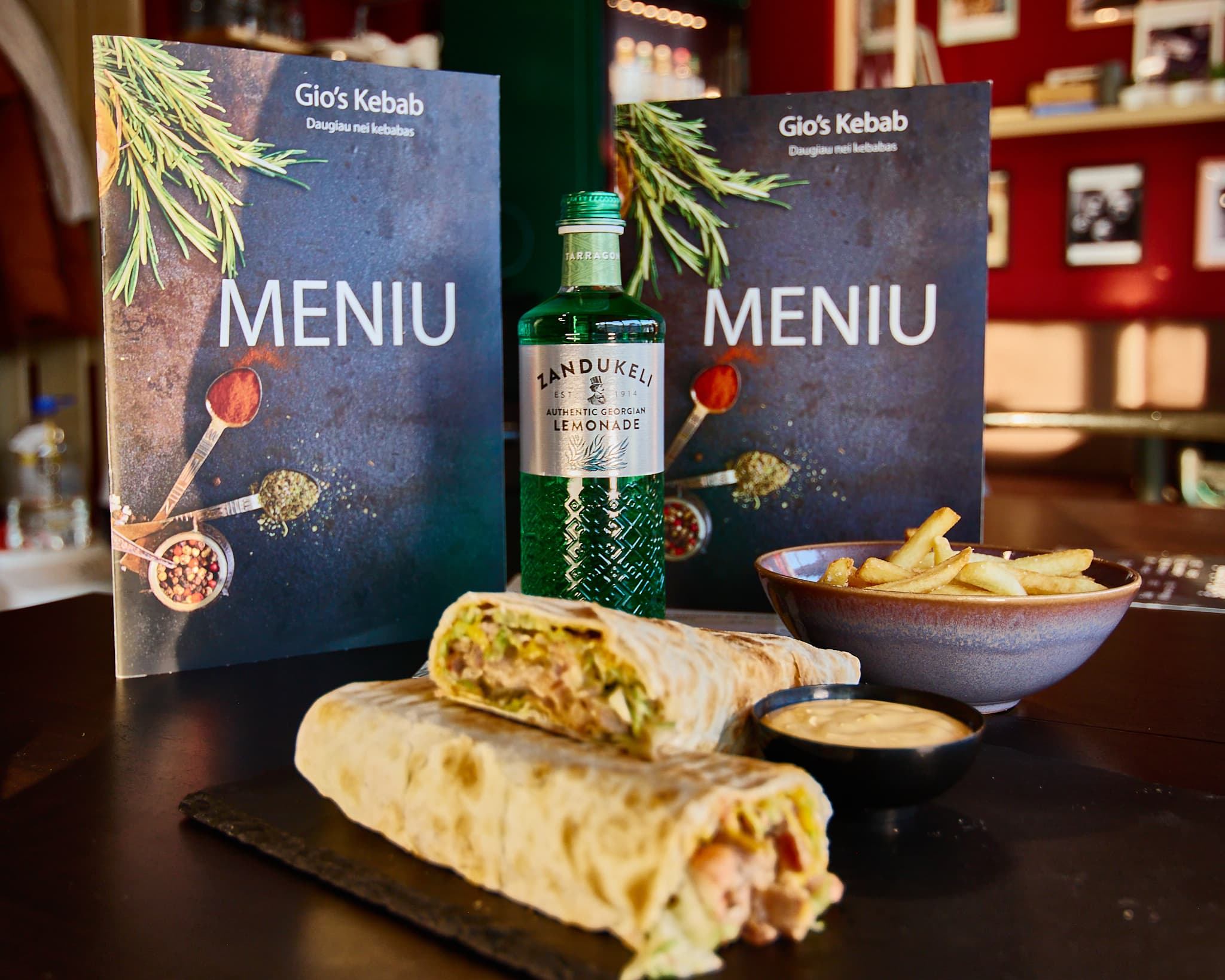 Ant stalo pateiktas kebabas, bulvytės, padažas ir gėrimas restorano aplinkoje