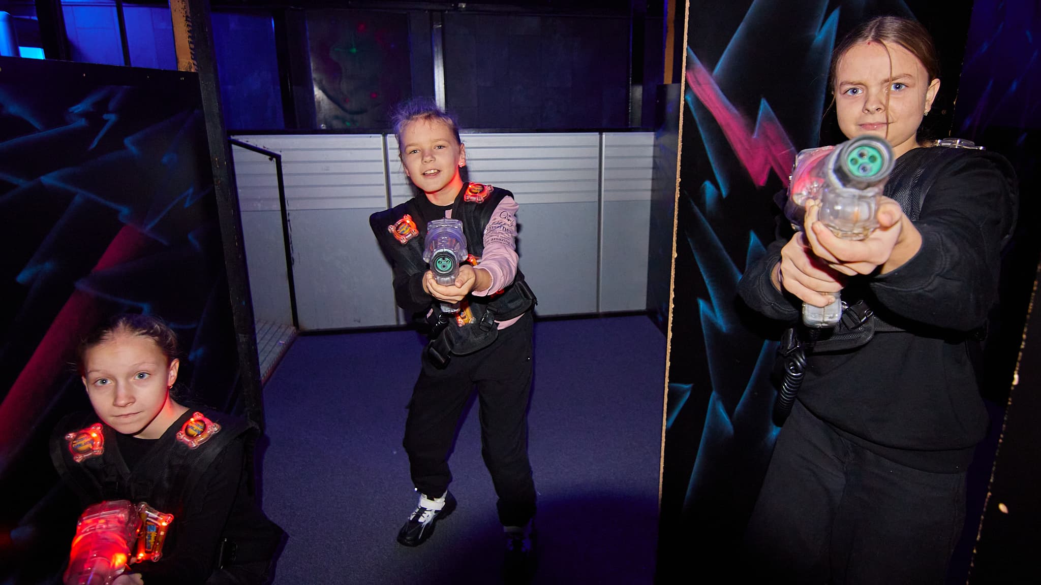 Trys vaikai su lazerių žaidimo ginklais žaidžia pramogų erdvėje