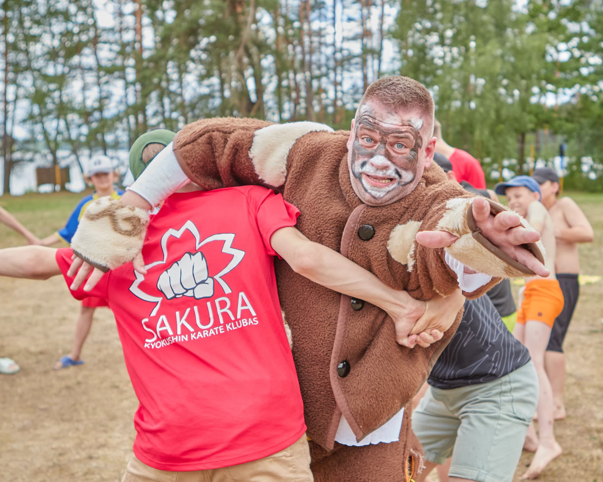 Lauko žaidimo metu suaugęs dalyvis ir vaikai atlieka judrią užduotį