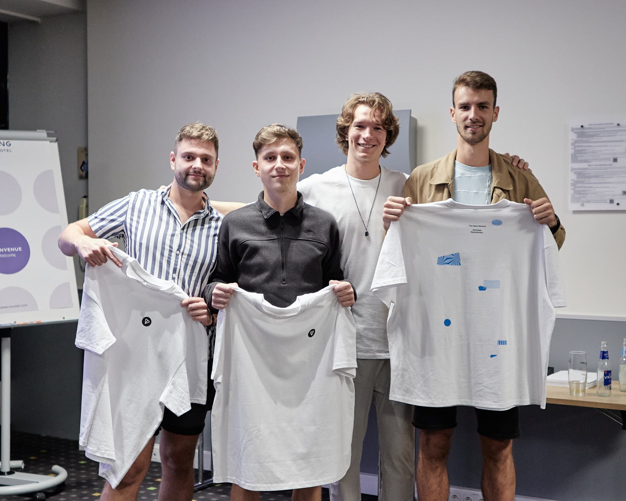 Keturi jauni vyrai po renginio pozuoja laikydami marškinėlius