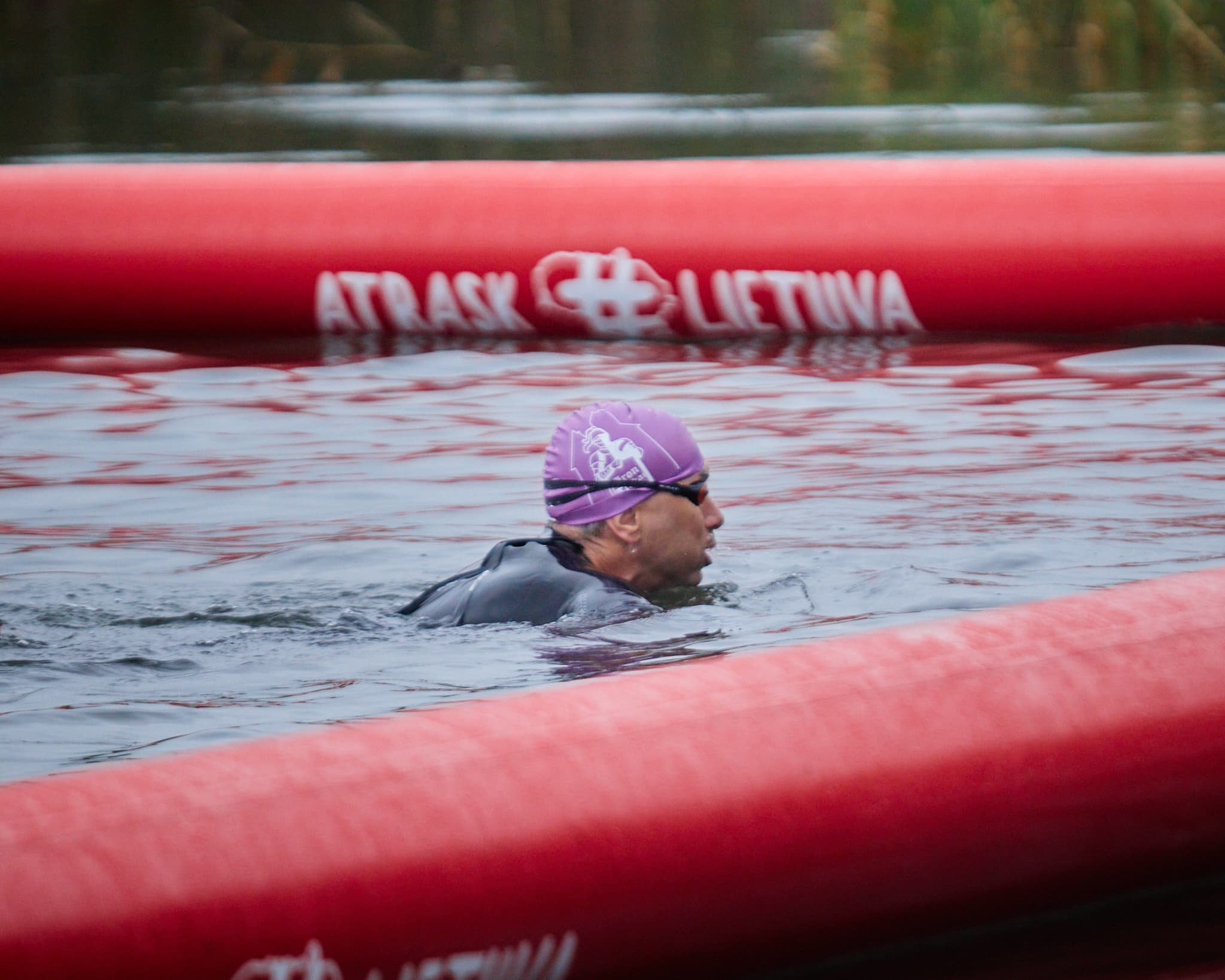 Triatlono dalyvis su plaukimo kepuraite plaukia pažymėtoje trasoje