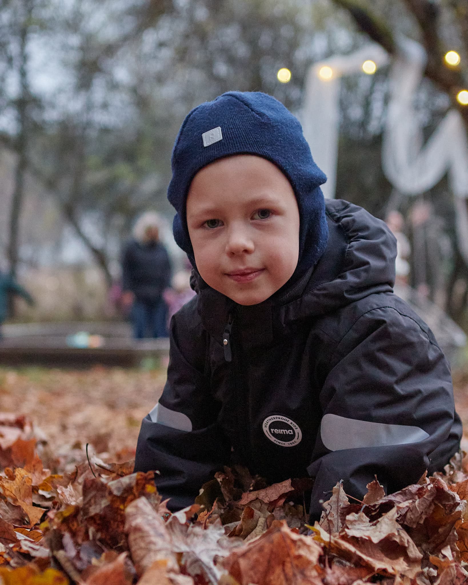 Mažas berniukas su mėlyna kepure guli rudeniniuose lapuose