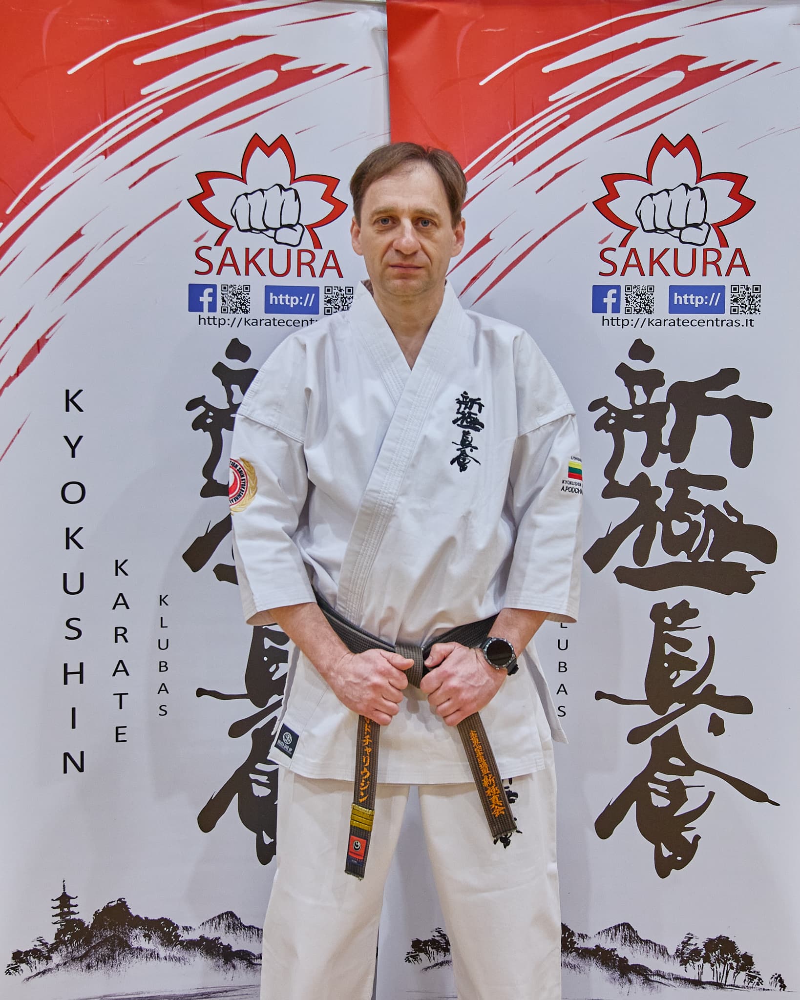 Vyras su balta karatė apranga pozuoja prie klubo stendų