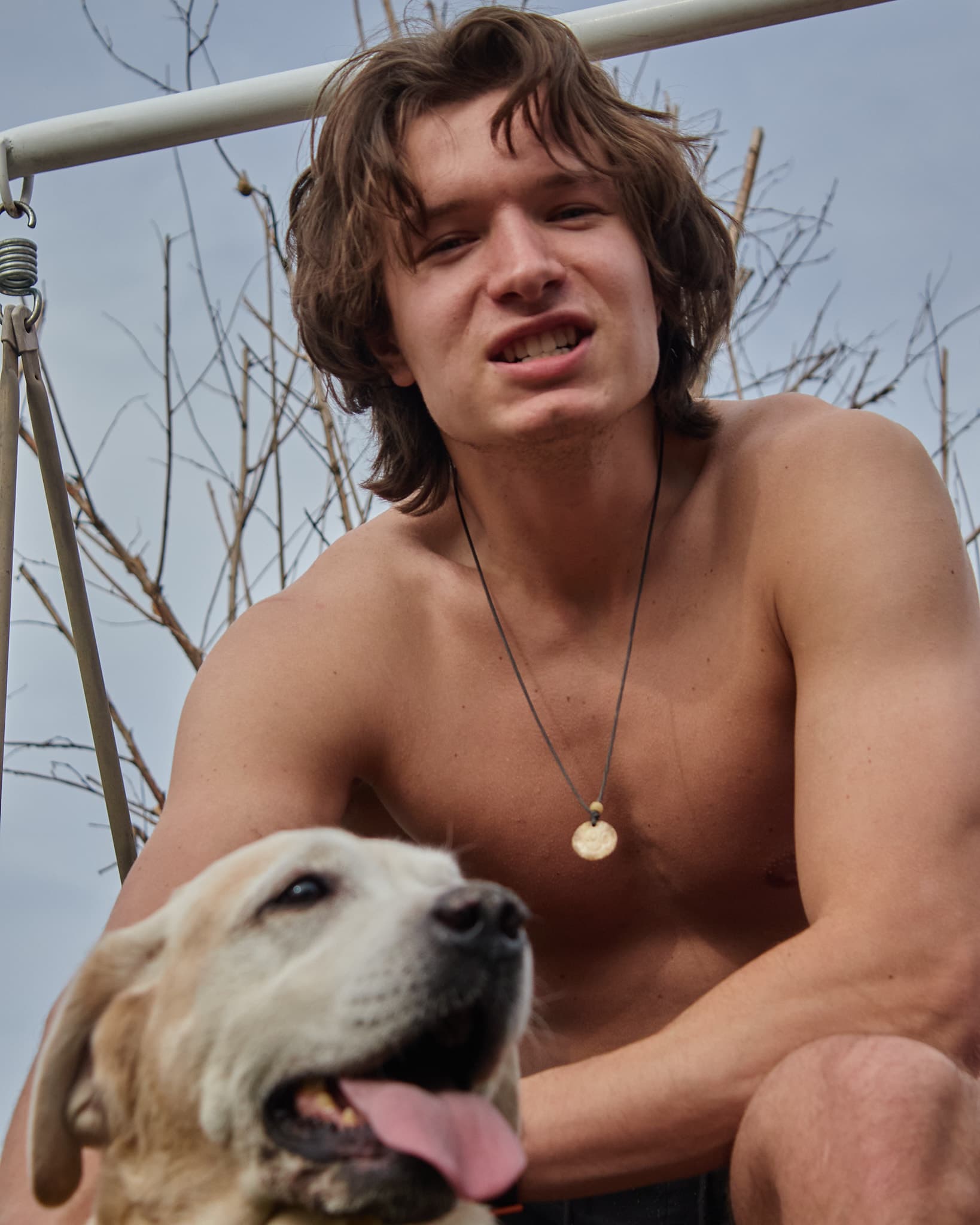 Jaunas vyras pozuoja lauke, pirmame plane matomas šuo